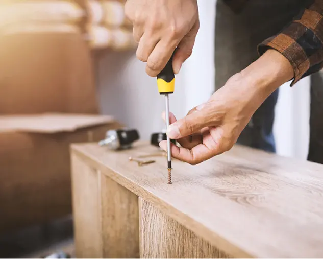 Nahaufnahme einer Hand, die mit Schraubendreher eine Schraube in ein Holzregal dreht. Symbolbild für Möbelmontage, Aufbauservice und fachgerechte Möbelinstallation im Wohnbereich.